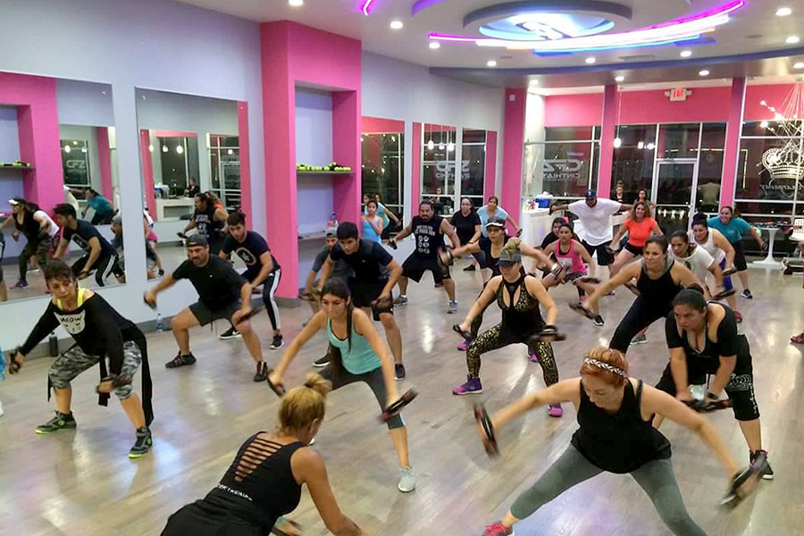 people working out in a group class at the Cinthia's fitness center with pink walls and ambient lighting.