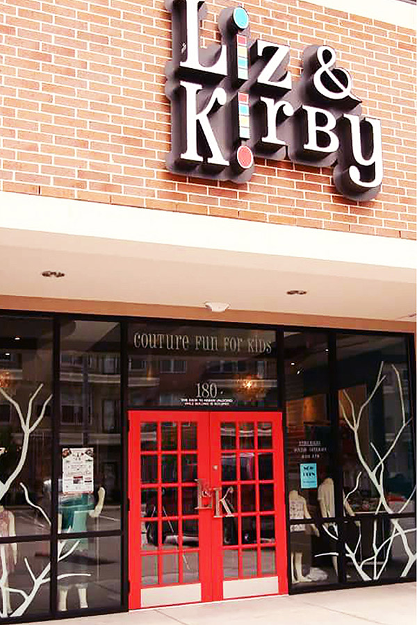 store front designed by Shundra Harris Interiors showing signage in serif font for Liz and Kirby children clothing store with double door with window panes in red color