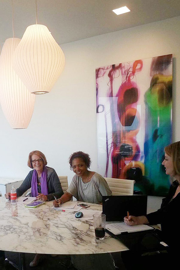Shundra Harris sitting at a table with other 3 other women and large colorful painting on the wall behind them