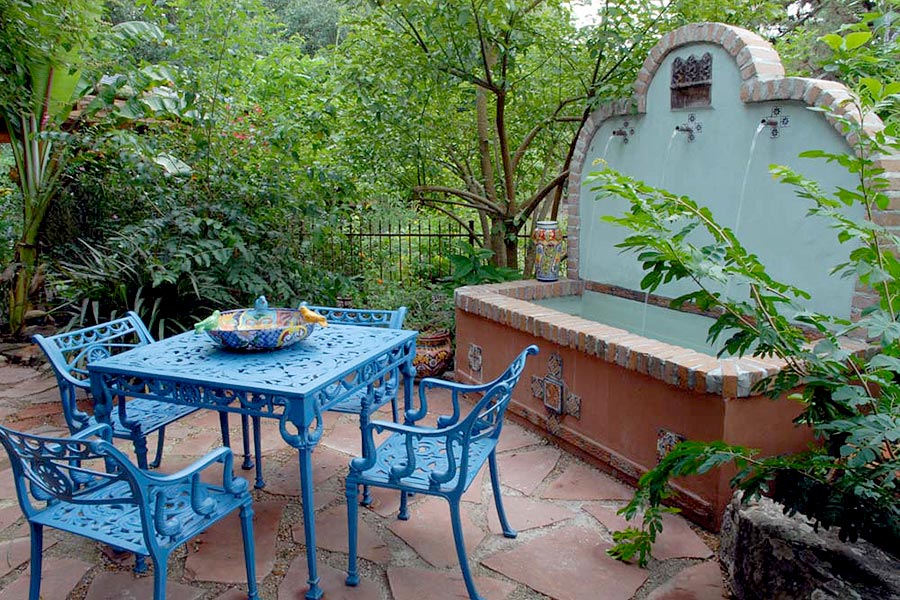 Patio furniture painted in blue set next to a water fountain in a paved courtyard.