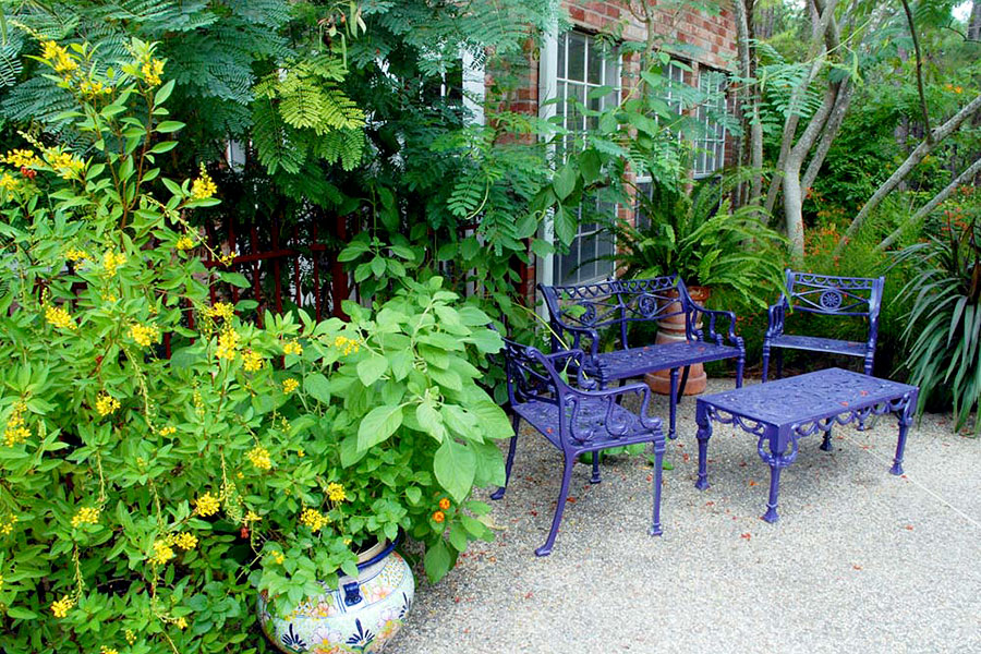 Out door seating with purple painted metal chairs and table against a full green foliage planted in pots and in the ground