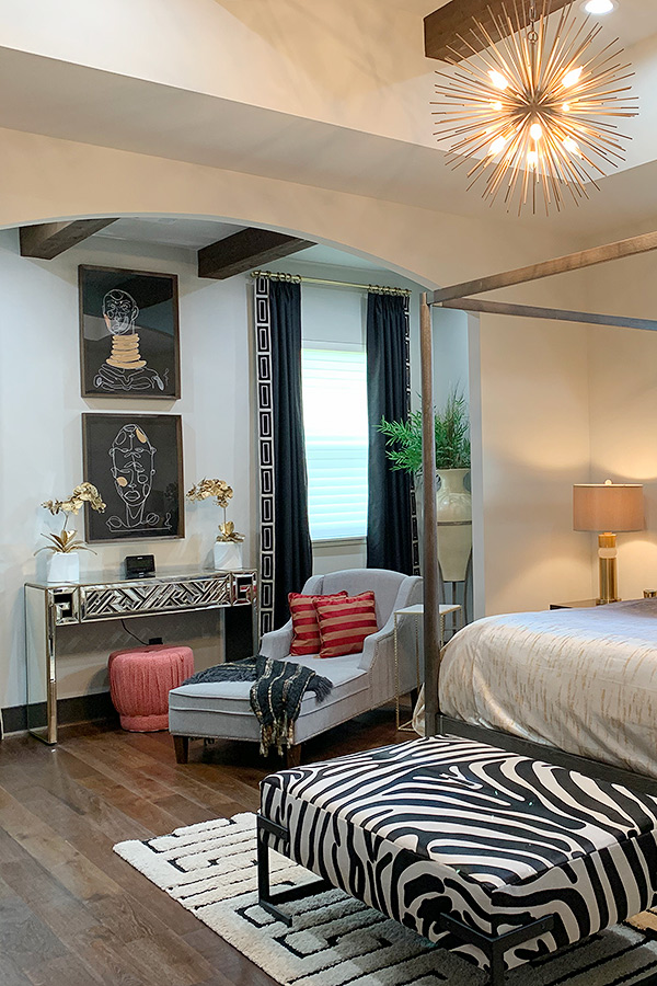 Bedroom with a zebra printed bench and matching console table and dark curtains lined with ethnic borders.