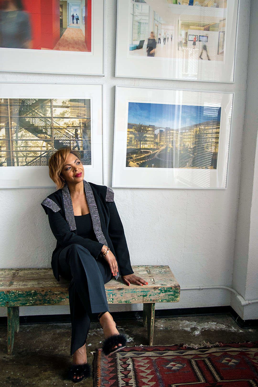 Shundra Harris interior designer sitting on bench against a wall with large framed photos of architectural buildings hung behind her.